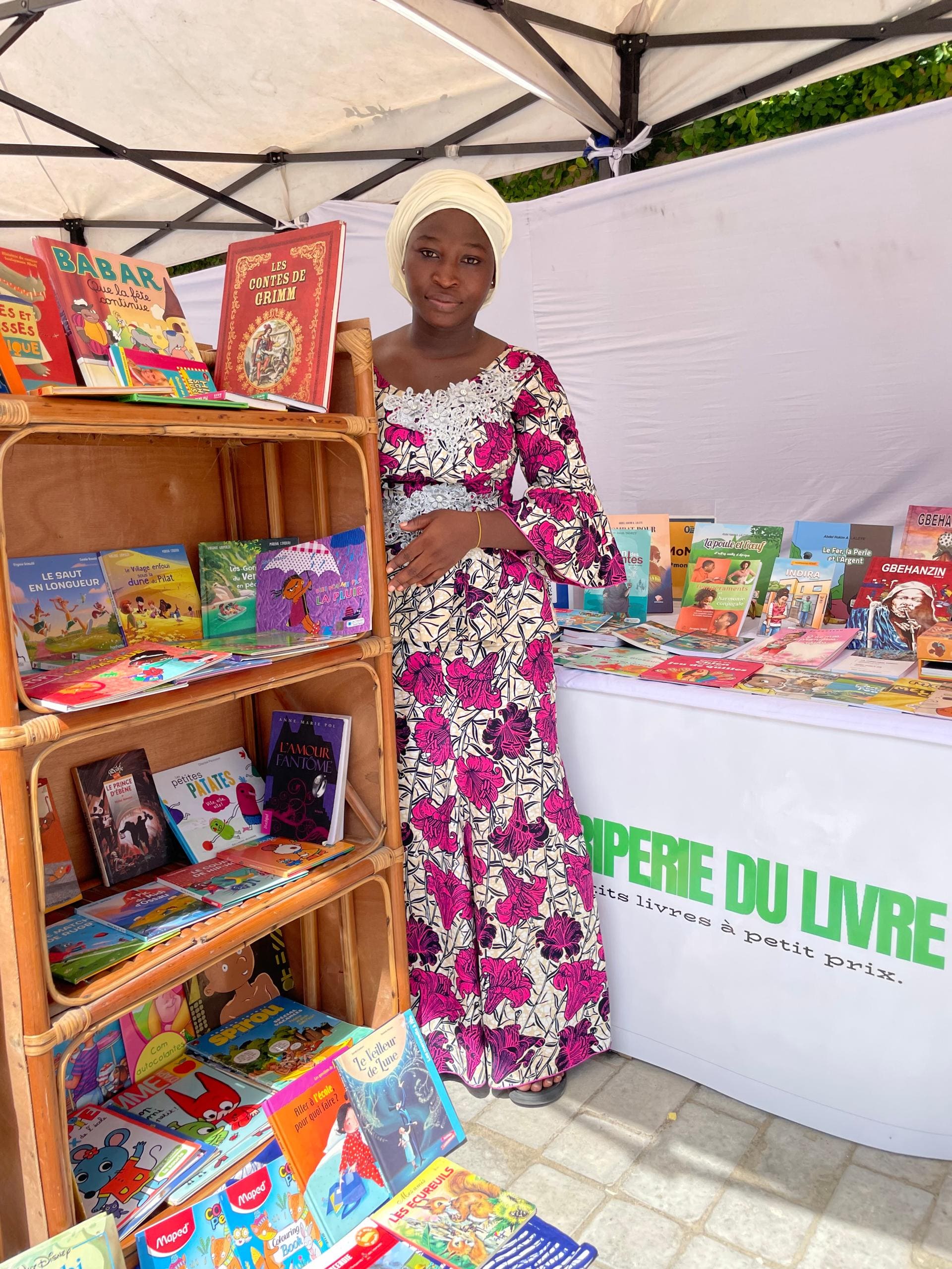 Vendeuse posant devant l'étagère et la bannière "La Friperie du Livre, petits livres à petit prix"